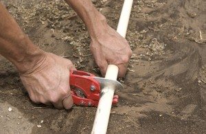 irrigation repair services. He is cutting out a broken section. The background is sand.